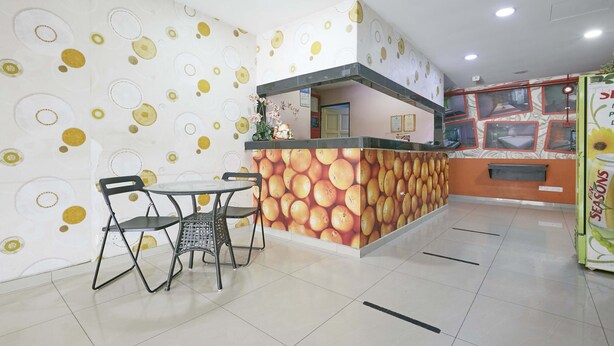 A reception area with a patterned wall, a counter with a fruit-themed backdrop, and a seating area with two chairs and a table. - Hotel O Orange Hotel Kuala Pilah (Kuala Pilah)
