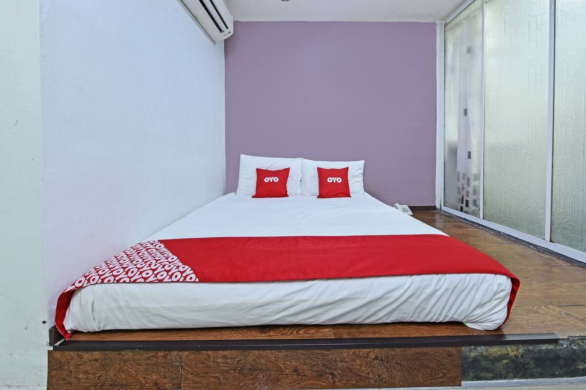 A neatly made bed with a red and white bedspread and pillows, a wooden headboard, and a sliding glass door to the right.