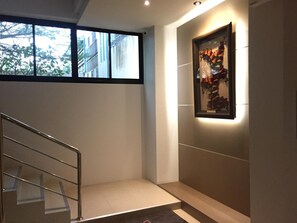 Un interior moderno con una escalera, una obra de arte enmarcada en la pared y una ventana que ofrece vistas a edificios y árboles.