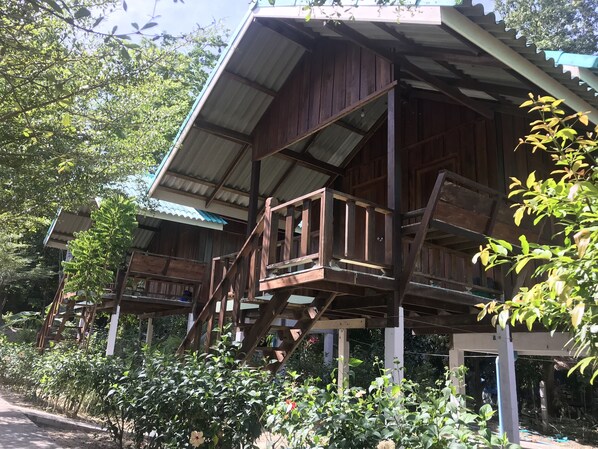 A wooden structure with a balcony and a covered area, surrounded by greenery.