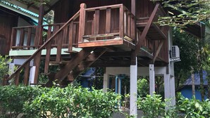 Eine Holzhütte mit Balkon und Treppe, umgeben von viel Grün.