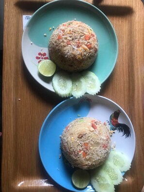 Two plates of fried rice with cucumber slices and lime wedges on a wooden table.