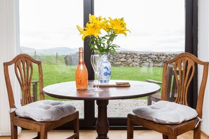 Una mesa de madera redonda con dos sillas, una botella de Dream, un florero con flores amarillas y un jarrón azul y blanco.
