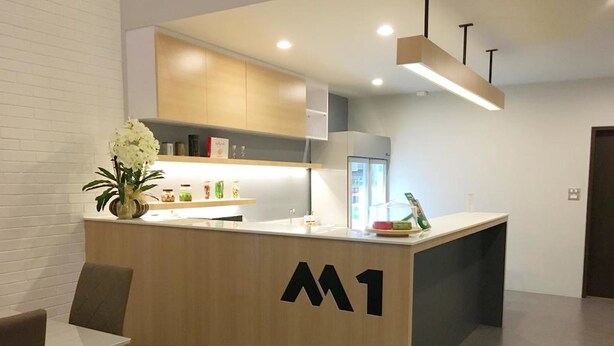 A modern reception area with a wooden counter, a vase of flowers, and a sign with the letter 'M'. - M-One Residence (Hat Yai)