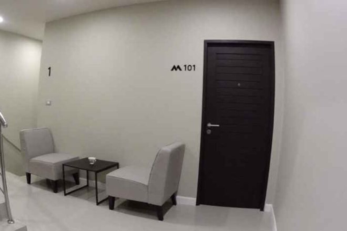 Un couloir avec une porte noire portant l’inscription « 101 », une petite table, deux chaises et un escalier.