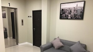 A modern interior with a grey sofa, two cushions, a black door, and a cityscape framed picture on the wall. - M-One Residence (Hat Yai)