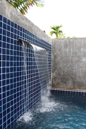 Una piscina con una cascada frente a un muro de azulejos.