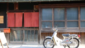 A motorcycle parked outside a building with a wooden door and windows. - Asuka Guest House - Hostel (Asuka)