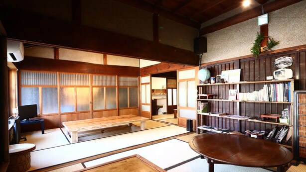 A traditional Japanese room with tatami flooring, a low wooden table, a bookshelf, and a television. - Asuka Guest House - Hostel (Asuka)