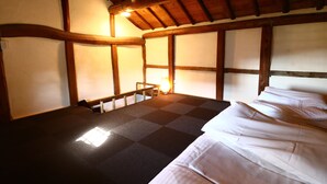 A room with a checkered floor, wooden beams, a bed with white linens, and a small table with a lamp. - Asuka Guest House - Hostel (Asuka)