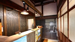 A reception area with a wooden counter, a ceiling fan, and a traditional sliding door. - Asuka Guest House - Hostel (Asuka)