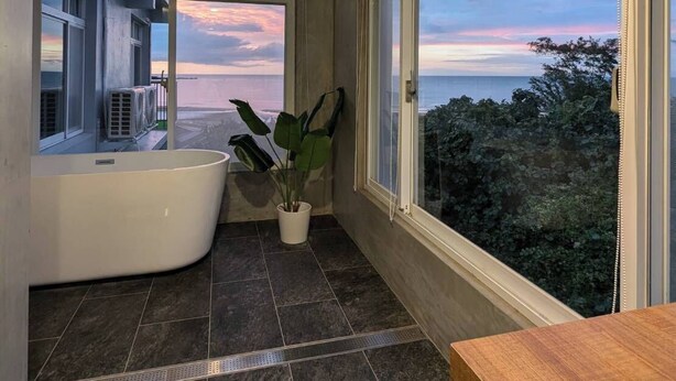 Une salle de bain moderne avec une baignoire sur pieds, une plante en pot et de grandes fenêtres donnant sur la mer.