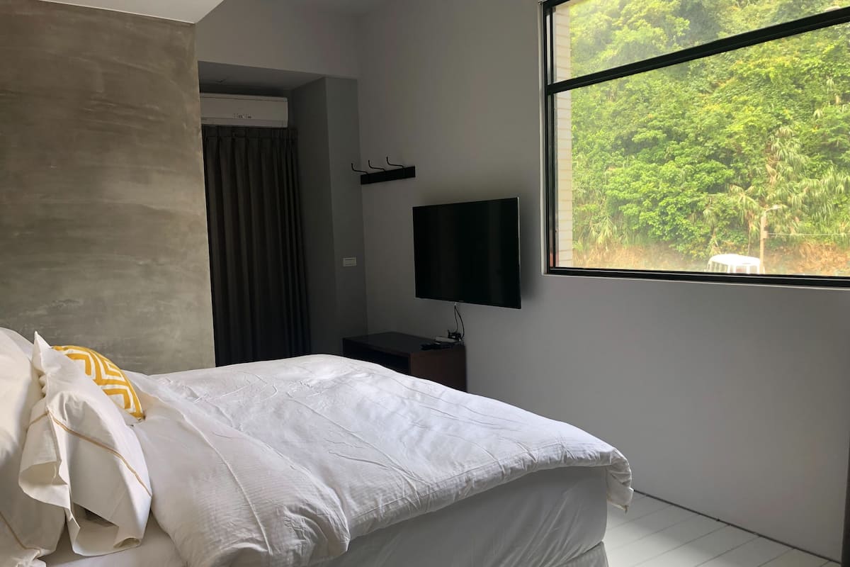 Een moderne hotelkamer met een bed, een flatscreen-tv, een raam met uitzicht op een bos en een ingebouwde airconditioning.