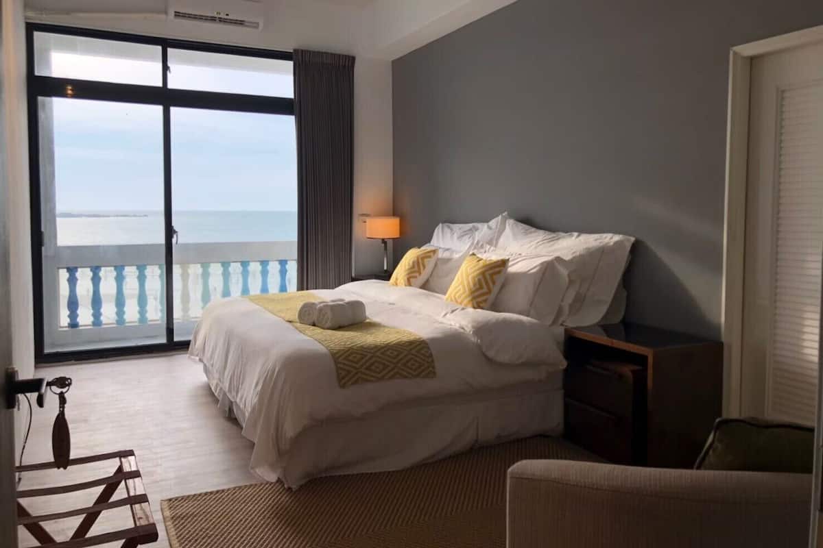 Hotelkamer met een groot bed, een nachtkastje, een lamp en uitzicht op zee door een schuifdeur.