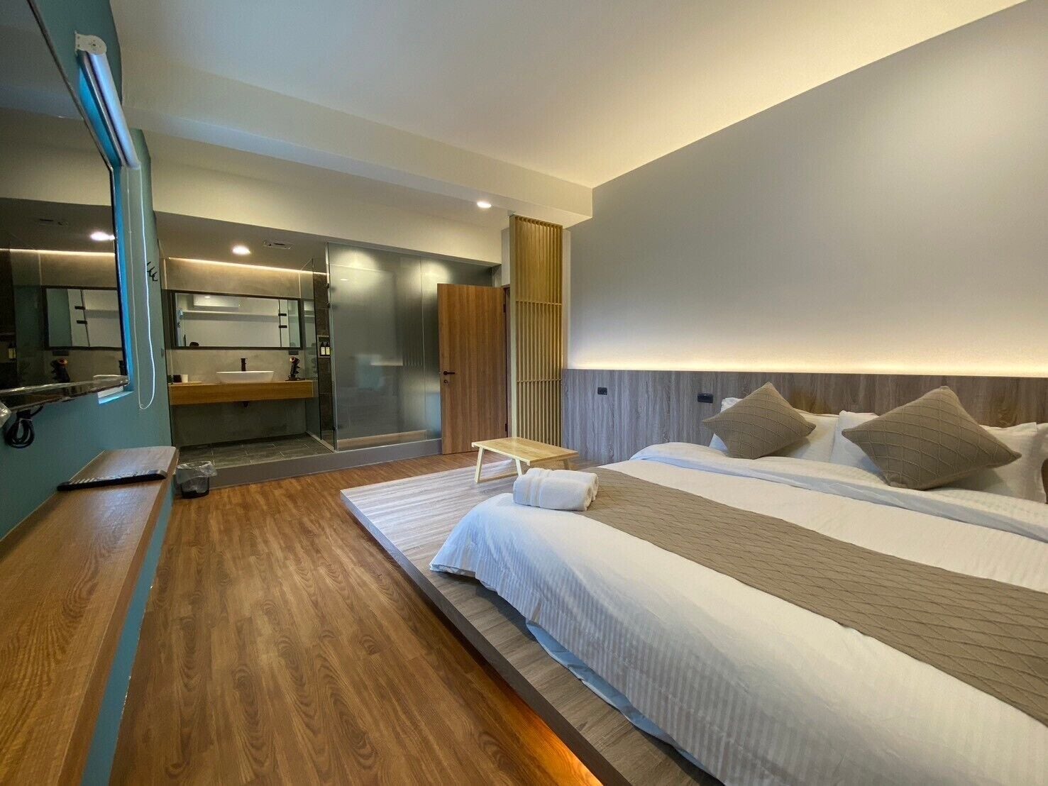 A modern hotel room with a large bed, a bedside table, a mirror, and a bathroom with a shower and sink.