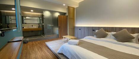 A modern hotel room with a large bed, a bedside table, a mirror, and a bathroom with a shower and sink.