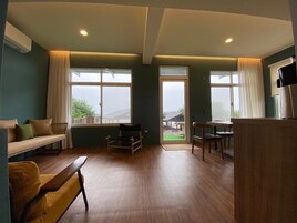Quarto espaçoso com piso de madeira, sofá, mesa de jantar com cadeiras e grandes janelas com cortinas.