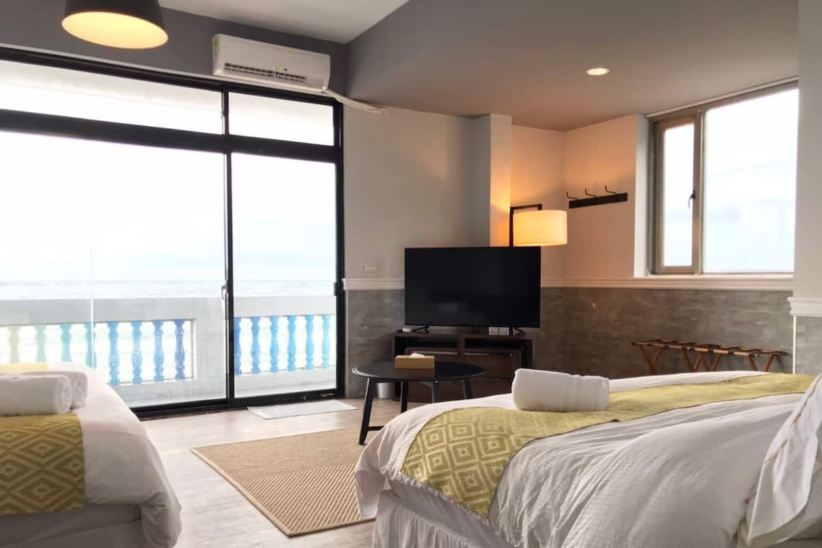 Een hotelkamer met twee bedden, een televisie, een balkon met uitzicht en een kleine tafel.