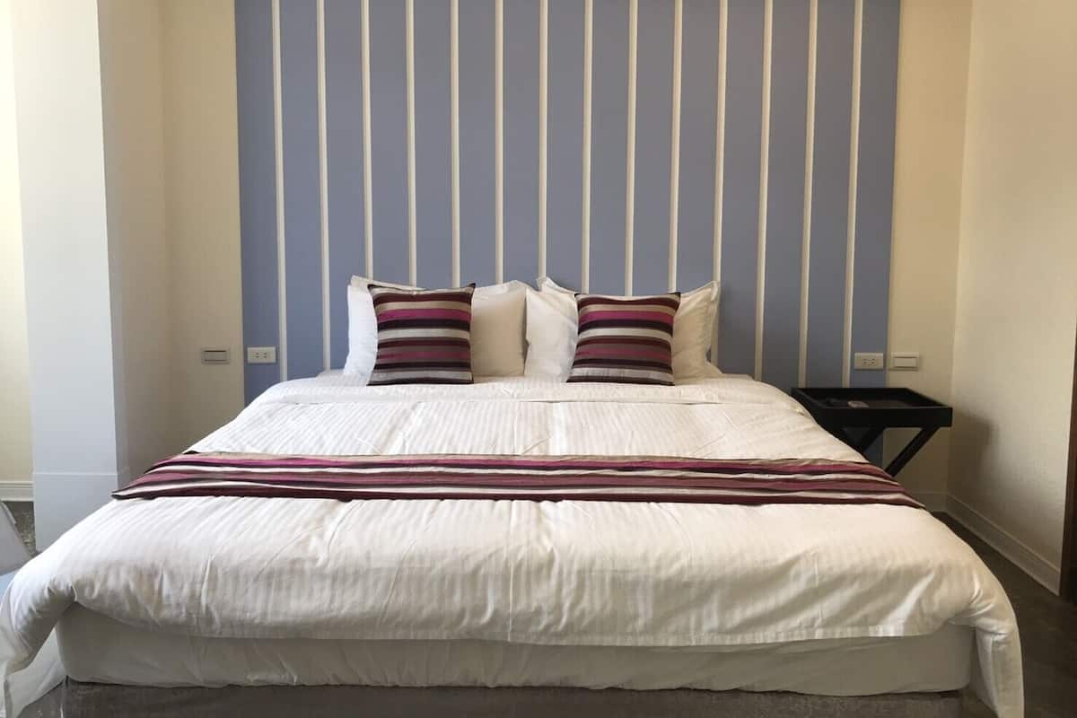 Een opgemaakt bed met wit beddengoed en twee gestreepte kussens, een zwarte nachtkastje met een dienblad, en een blauw gestreept hoofdbord.