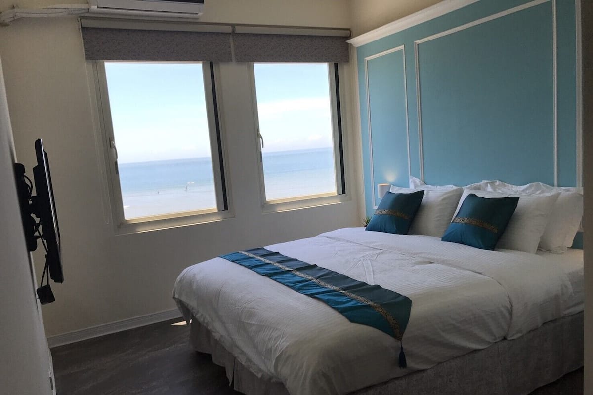 Een slaapkamer met een bed, twee ramen en uitzicht op zee.