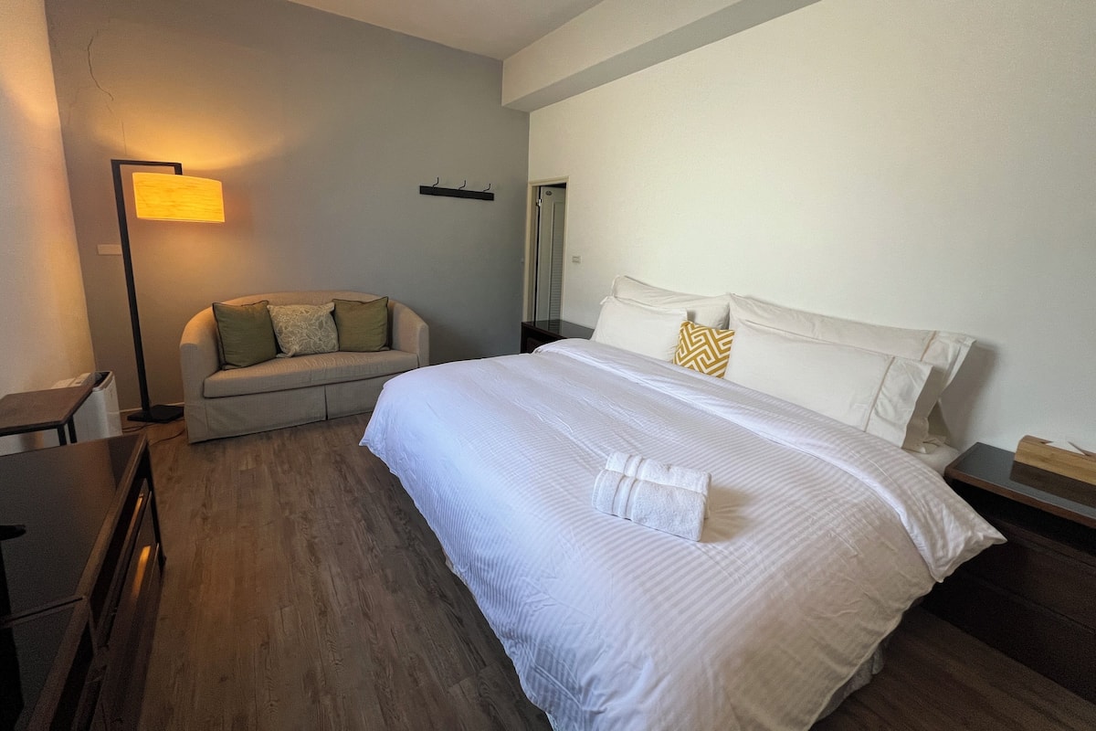 Een hotelkamer met een groot bed, een slaapbank, een vloerlamp en een houten vloer.