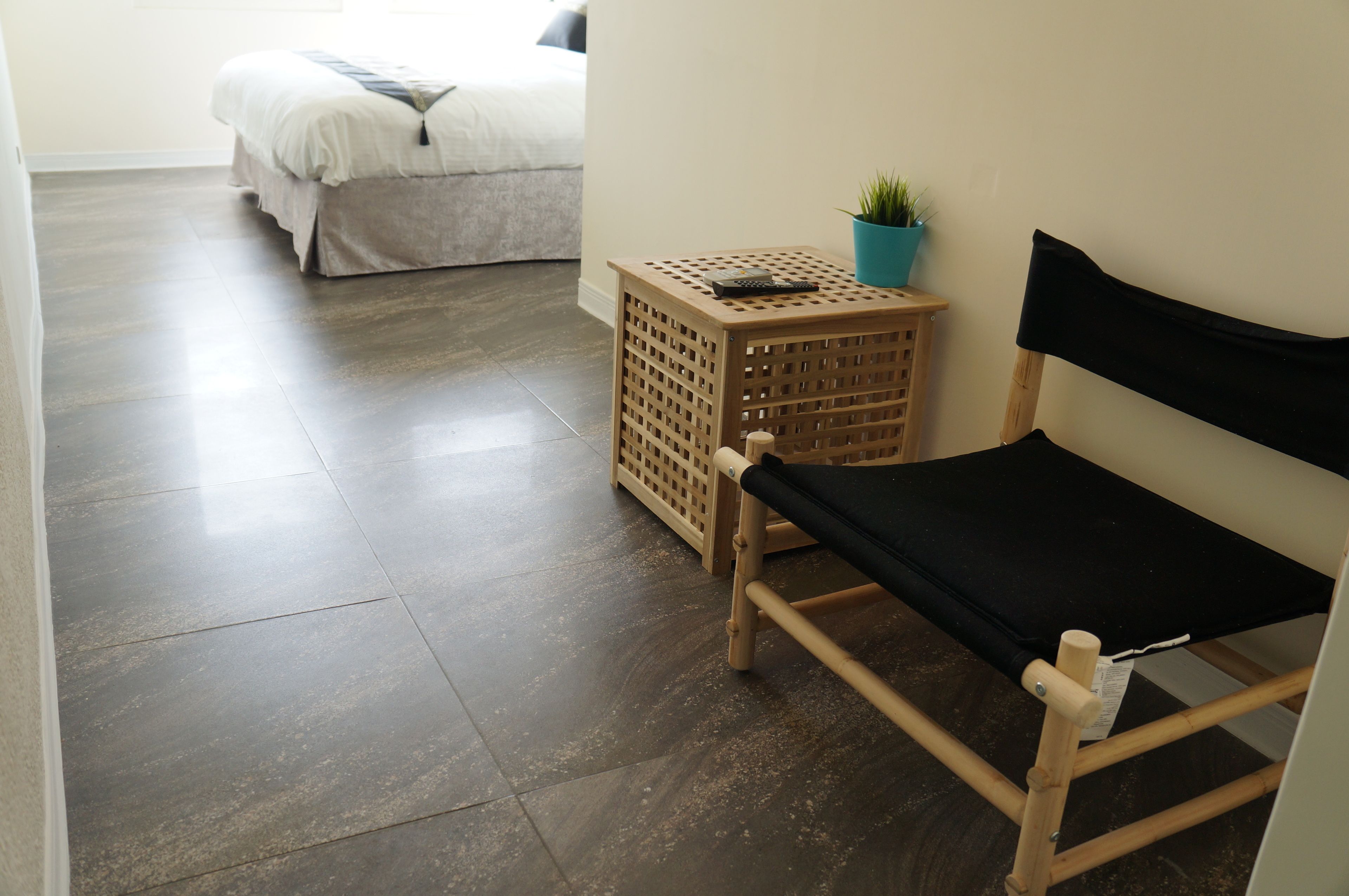 A room with a bed, a small wooden table with a plant, and a bench.