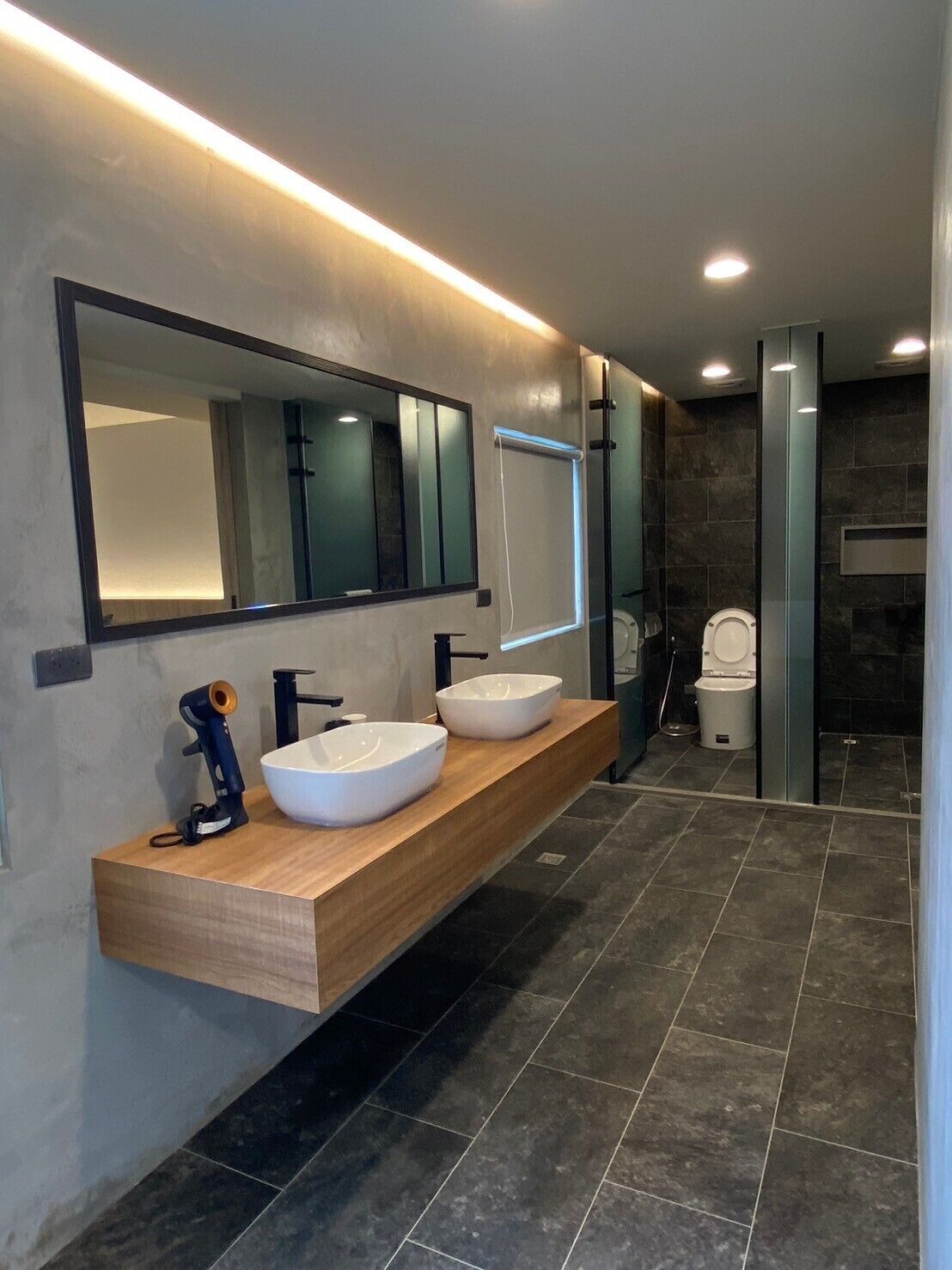 Un baño moderno con dos lavamanos blancos tipo sobreencimera, un espejo grande y un inodoro.