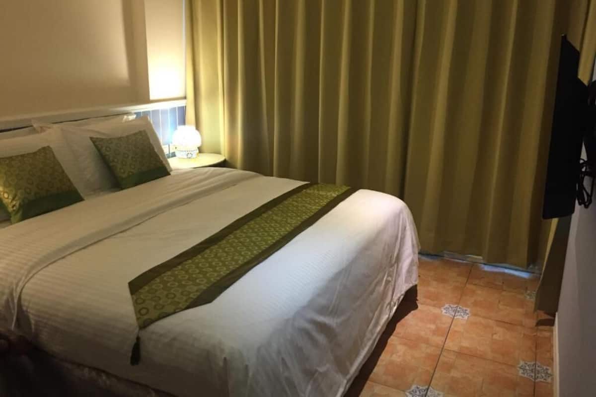 Een hotelkamer met een bed, gordijnen, een nachtkastje met een lamp en een betegelde vloer.