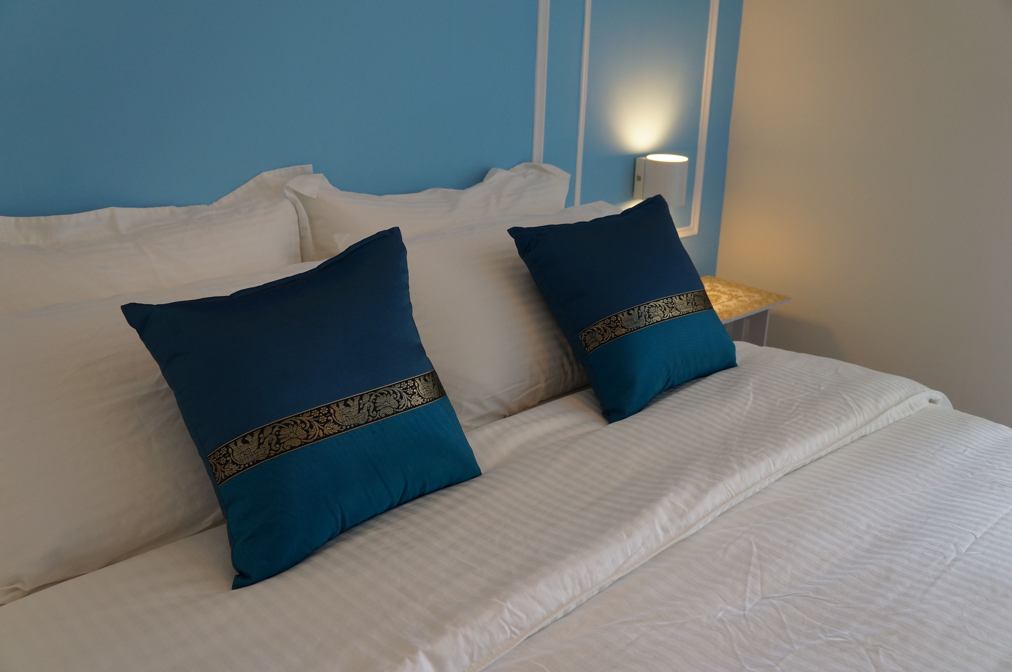 A bed with white bedding and two dark blue pillows with gold trim.