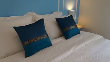 A bed with white bedding and two dark blue pillows with gold trim.