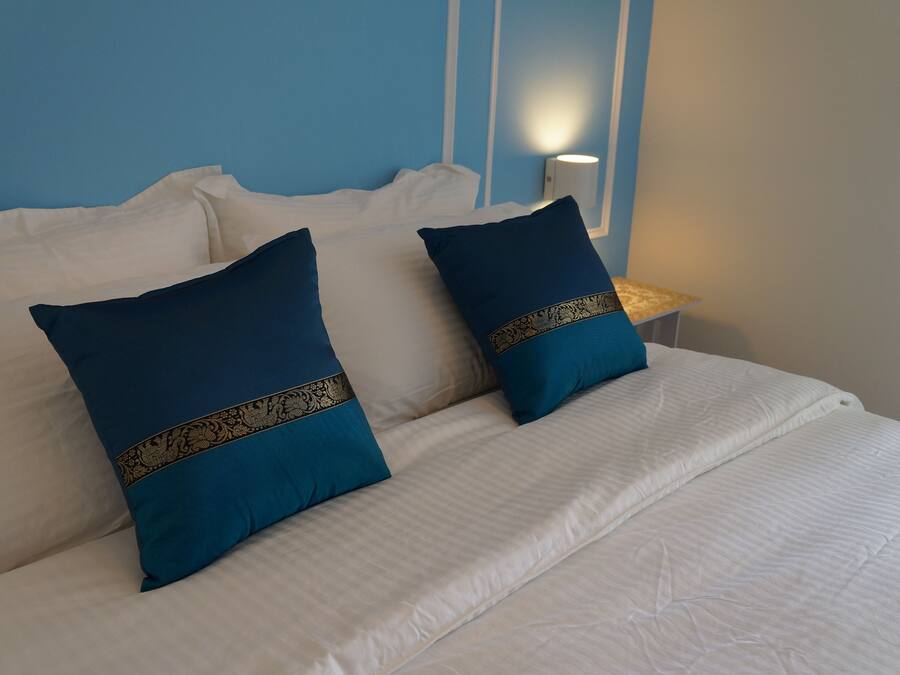 A bed with white bedding and two dark blue pillows with gold trim.