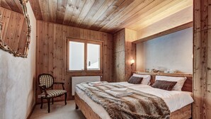 A wooden-paneled bedroom with a large bed, a chair, and a window. - Chalet les Marmottes - La Tzoumaz, 4 Vallees (La Tzoumaz)