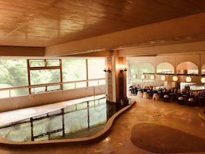 Una piscina interior con zona de bancos, rodeada por un bar y asientos.
