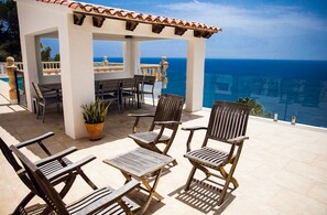 Une terrasse dotée de mobilier en bois et agrémentée d’une plante en pot, offrant une vue panoramique sur l’océan.