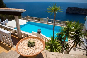 Une piscine avec vue sur la mer, entourée d’une balustrade blanche et de palmiers.