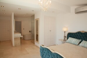 Une chambre à coucher avec un grand lit, un lustre, une table de chevet avec une lampe, et une salle de bain avec un lavabo et des toilettes.