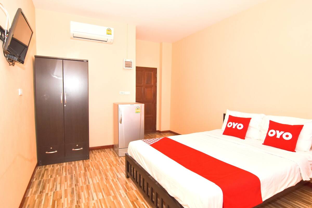 A hotel room with a bed, a wardrobe, a refrigerator, and a television mounted on the wall.