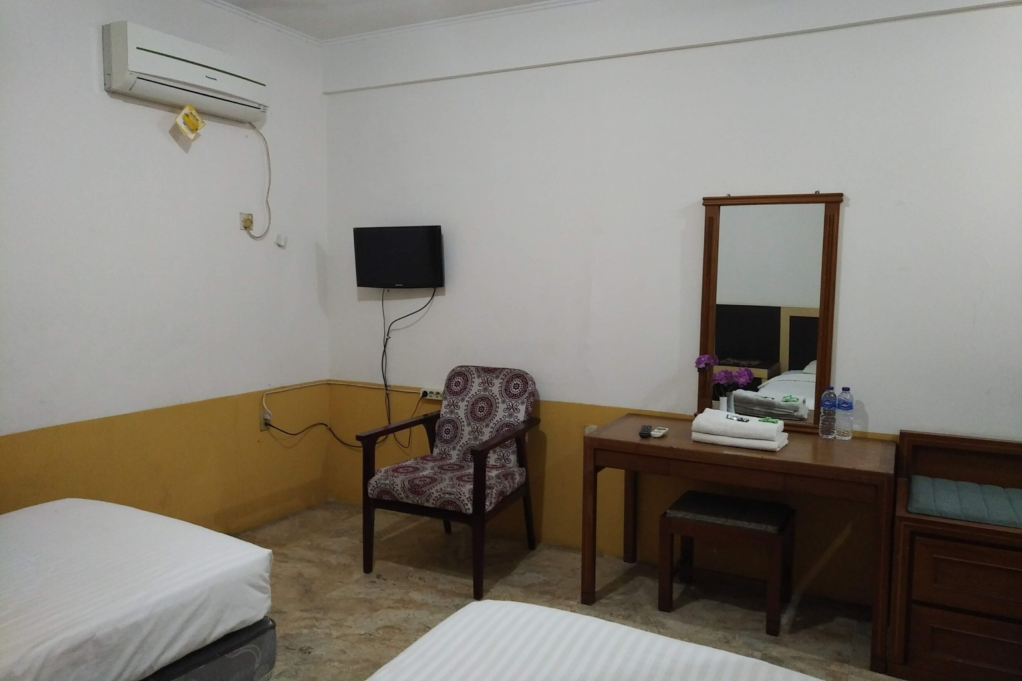Una habitación de hotel con una cama, un escritorio con silla, un televisor, un espejo y un aire acondicionado.