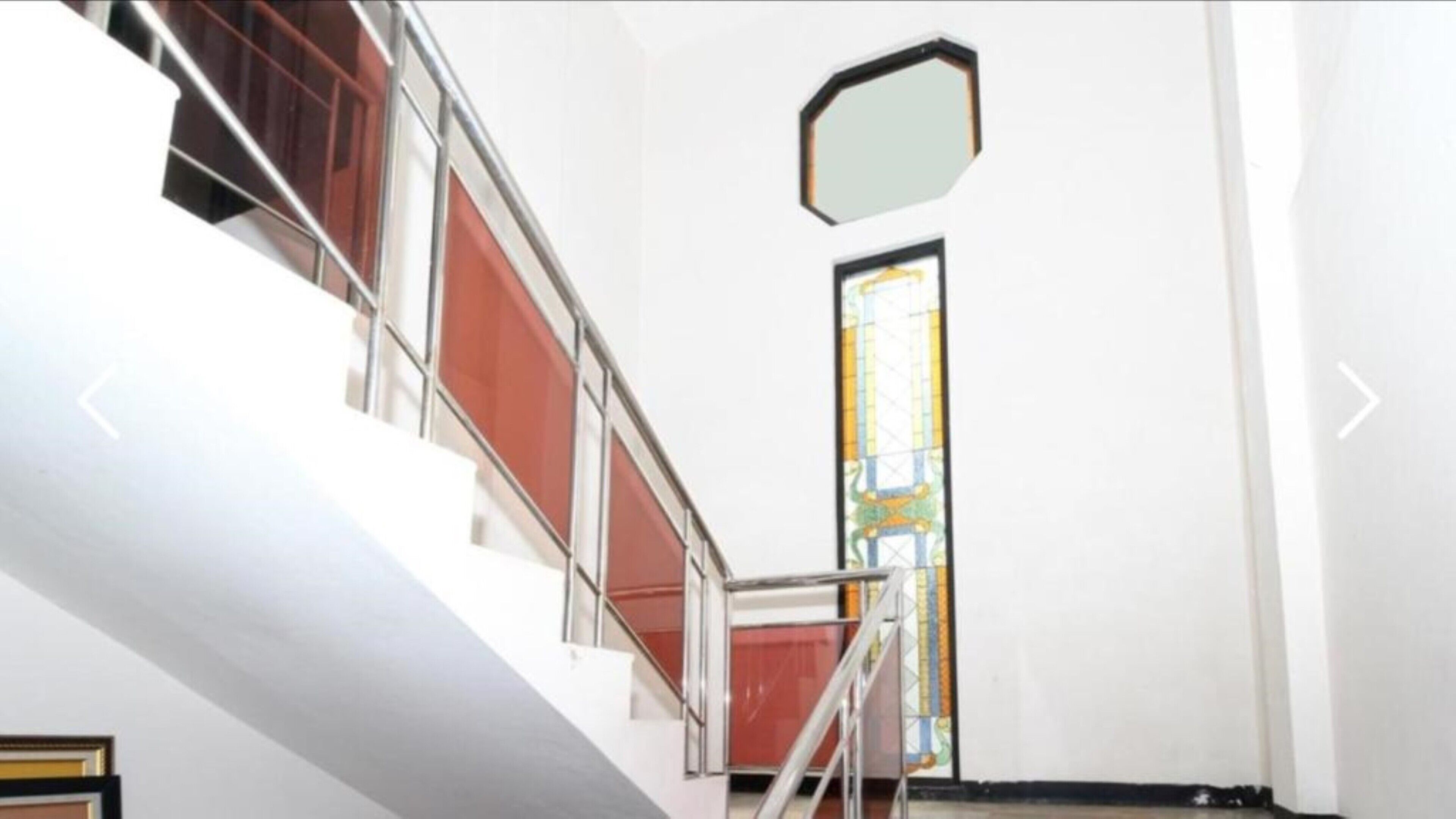 Un escalier avec une rampe en métal, une porte ornée d’un vitrail et un mur blanc.