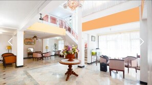 Un vestíbulo amplio con una mesa redonda central, varias zonas de estar, una escalera y un candelabro.