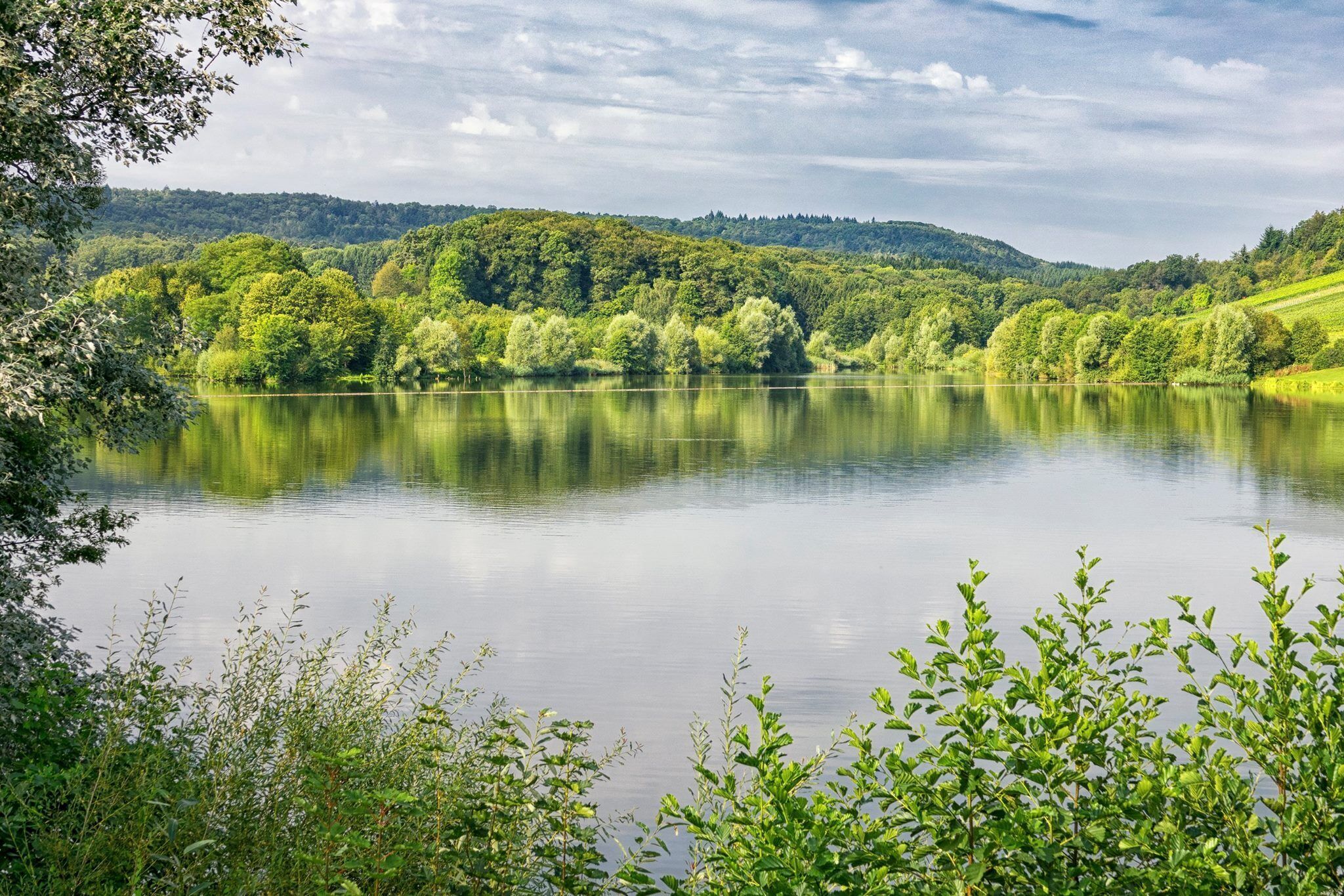 A calm lake surrounded by lush greenery and hills.
