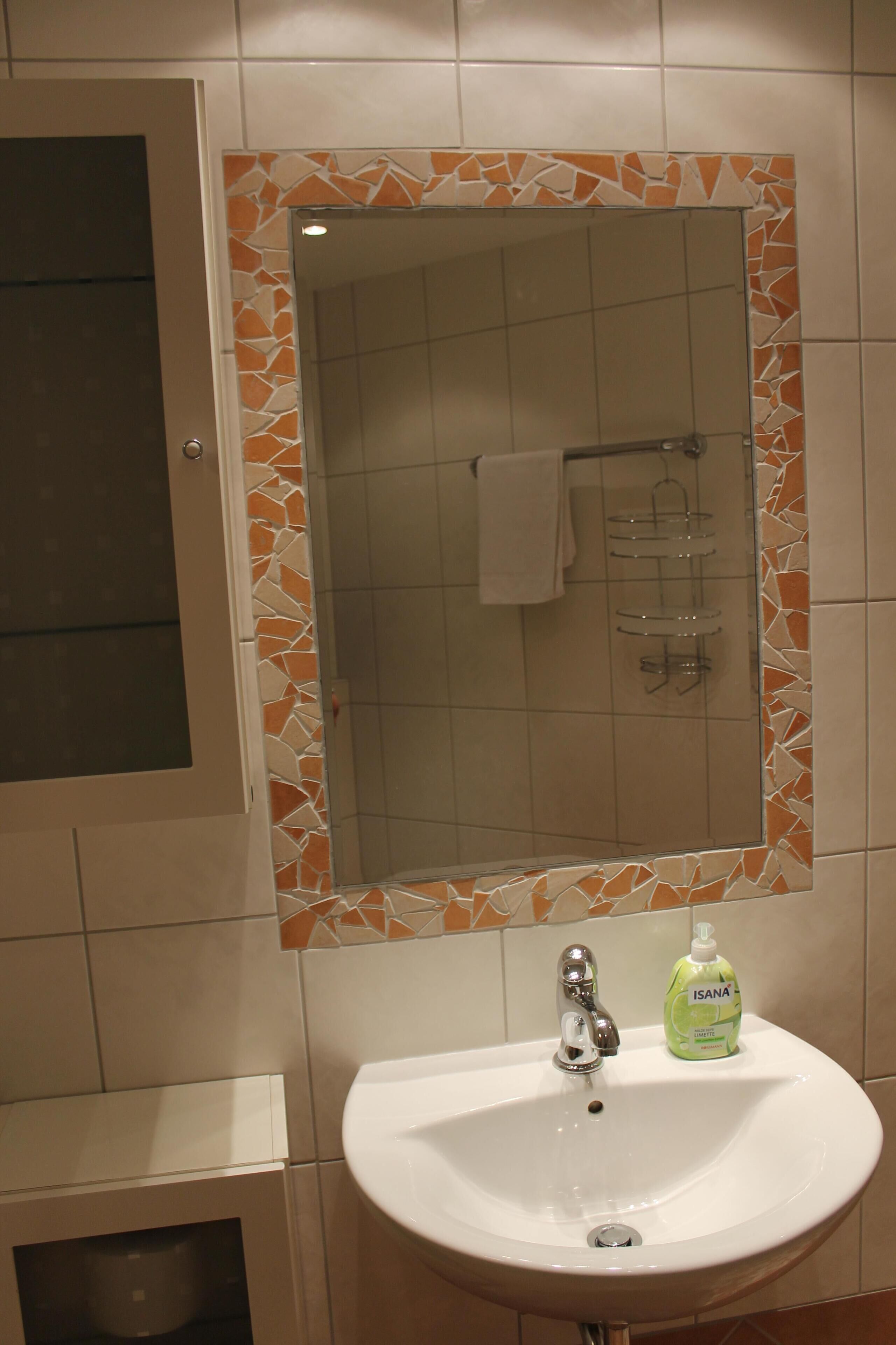 A bathroom with a white sink, a mirror with a mosaic frame, and a shower area.