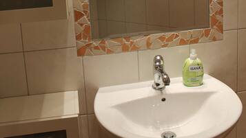 A bathroom with a white sink, a mirror with a mosaic frame, and a shower area.