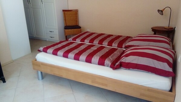 Un lit avec un cadre en bois, un matelas blanc et des oreillers à rayures rouges et blanches.