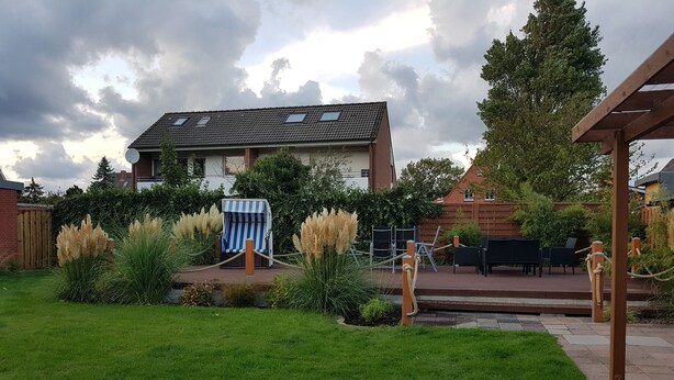 A residential backyard with a grassy lawn, a blue and white striped chair, and a patio area with outdoor furniture. - Casa mia: Gloria - Beautiful apartment with fireplace and terrace/ 2 bedrooms 2 bathrooms (Borkum)