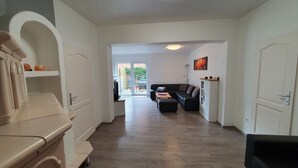 A modern living room with a black sectional sofa, a wooden coffee table, and a kitchen area with a white stove. - Casa mia: Gloria - Beautiful apartment with fireplace and terrace/ 2 bedrooms 2 bathrooms (Borkum)
