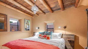 Un dormitorio con techo de madera, una cama con una manta roja, dos lámparas de pared y un cuadro en la pared.