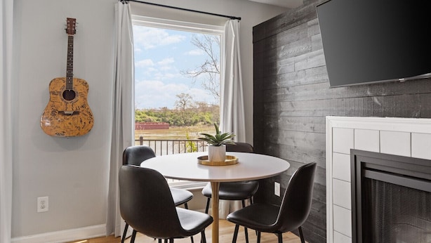 Una sala de estar moderna con una mesa redonda, sillas negras, una guitarra, un televisor y una chimenea.