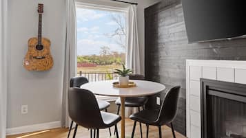 Un salon moderne avec une table ronde, des chaises noires, une guitare, un téléviseur et une cheminée.