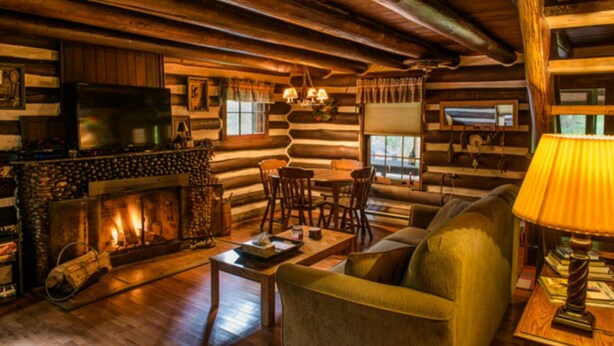 A log cabin interior with a fireplace, wooden furniture, and a television. - River’s Edge Cabin- Perfect for Romance/Outdoor Adventures/Relaxation (Elkins)